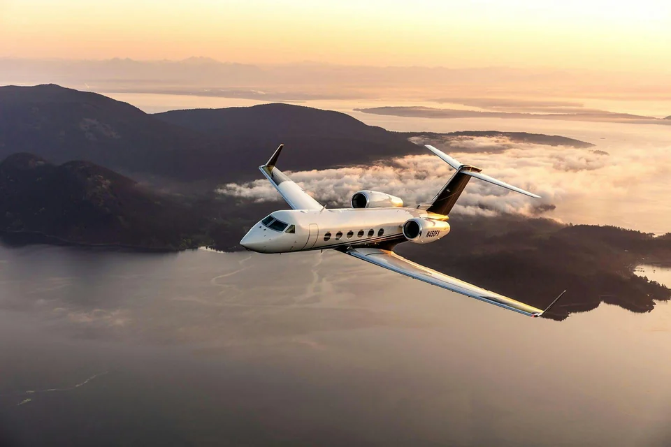 Business jet in flight above a coastal landscape in warm evening light, viewed from the front and above